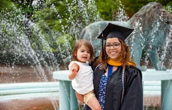 woman in graduation garb with her child in front of the lion fountain